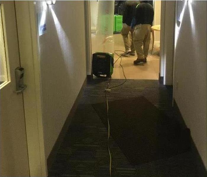 Image of workers placing drying equipment in hotel hallway to begin with drying process. 